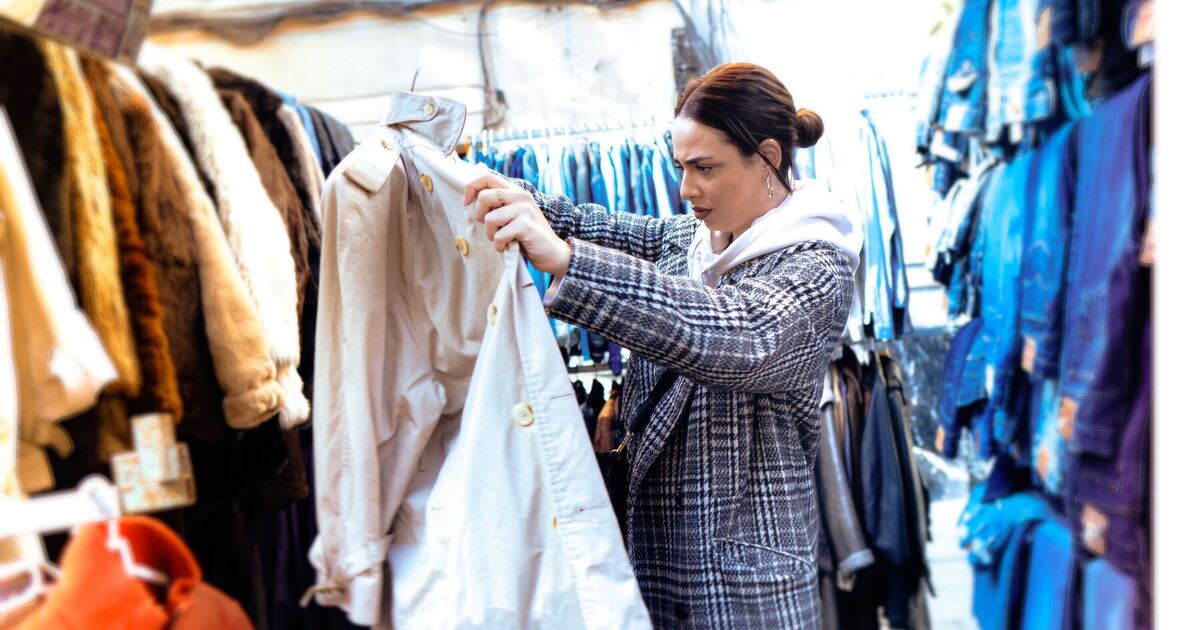** Hand holding gold jewelry and necklaces against white background in charity shop