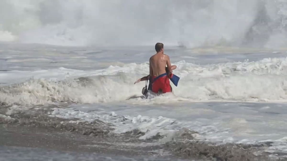 Teen lifeguard pulling young boy from crashing ocean waves in Santa Cruz California