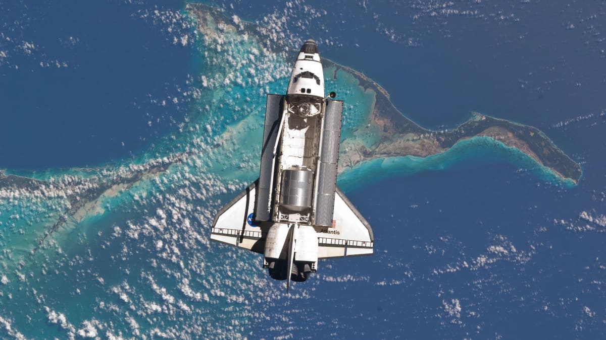 Space shuttle Atlantis with open cargo bay approaching International Space Station over Bahamas