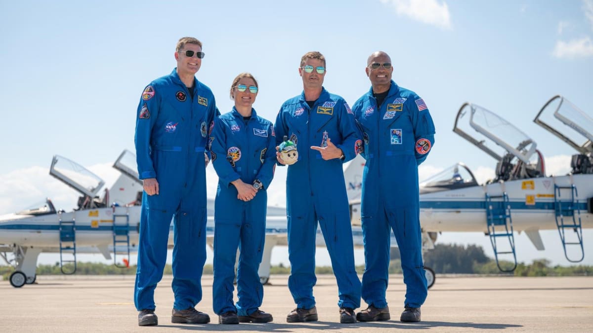 Four Artemis 2 astronauts pose with Rise, a smiling moon plush toy wearing Earth cap