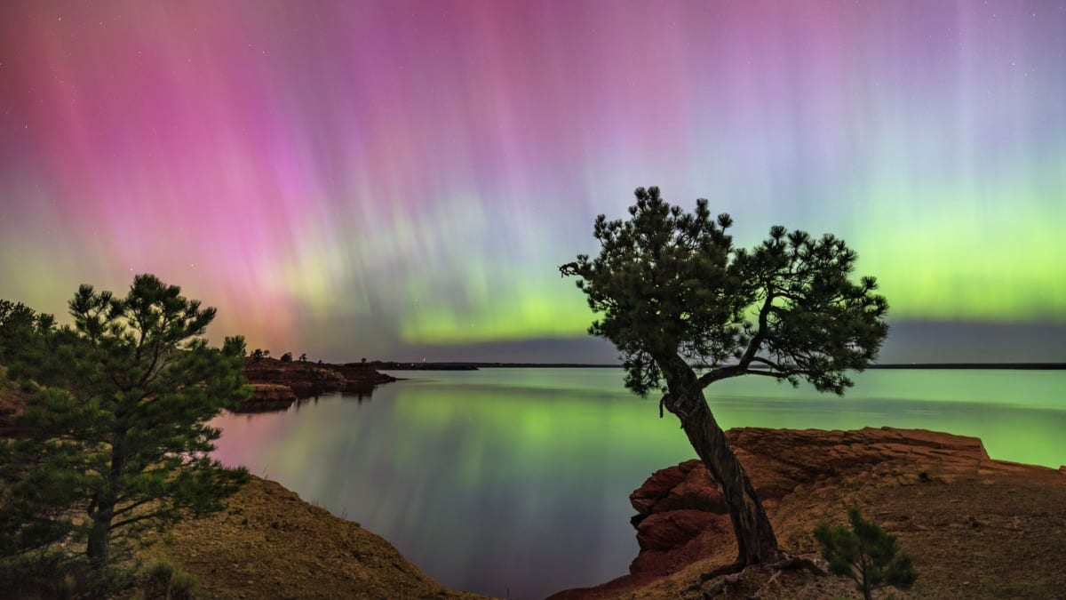 Green and purple northern lights dancing over dark night sky and landscape