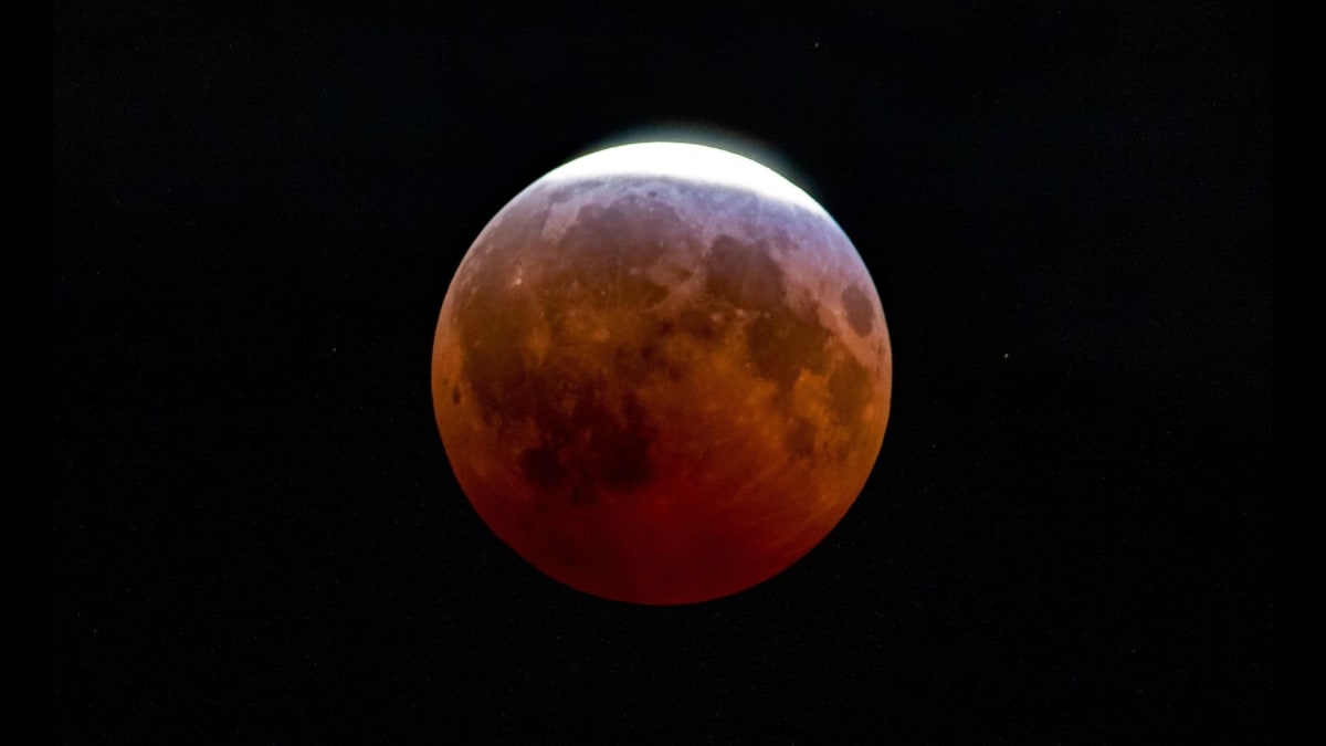 Deep red almost blood moon glowing against dark night sky during partial lunar eclipse