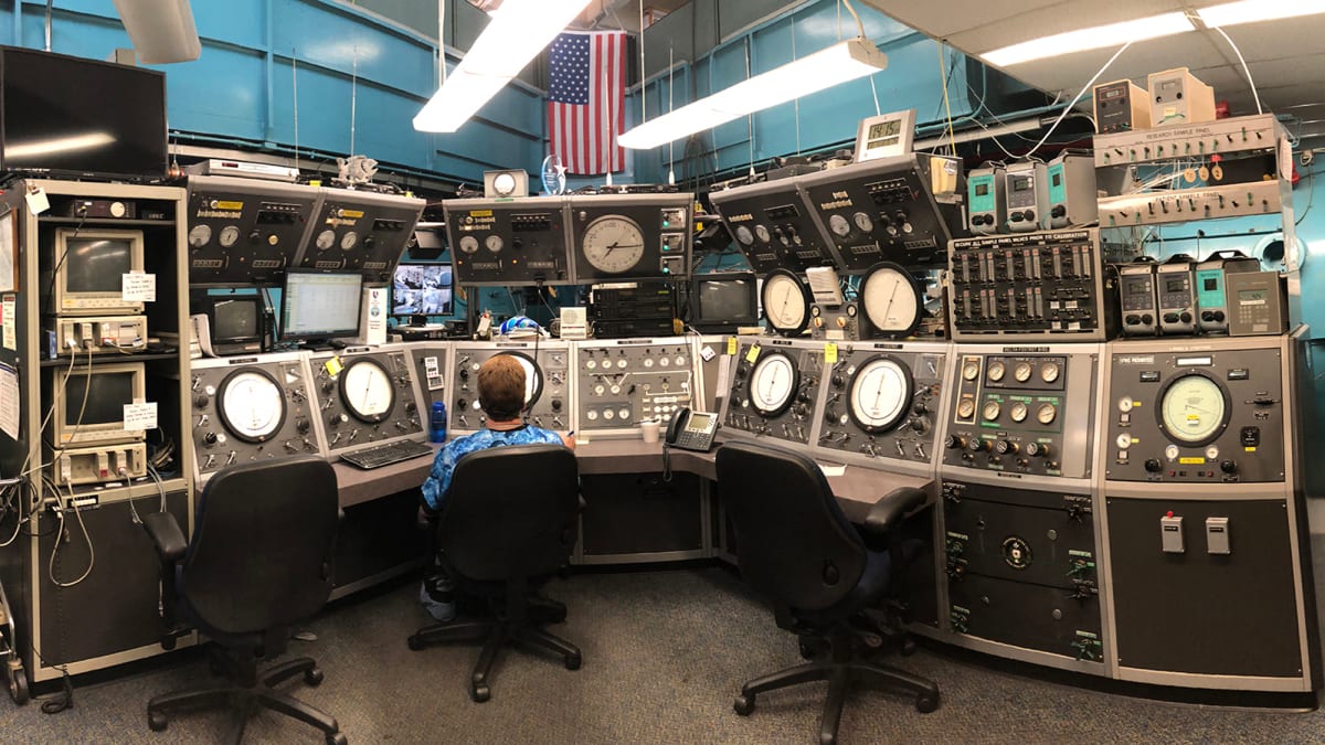 Researcher in blue coveralls stands inside Duke University's large cylindrical hyperbaric chamber used for diving experiments