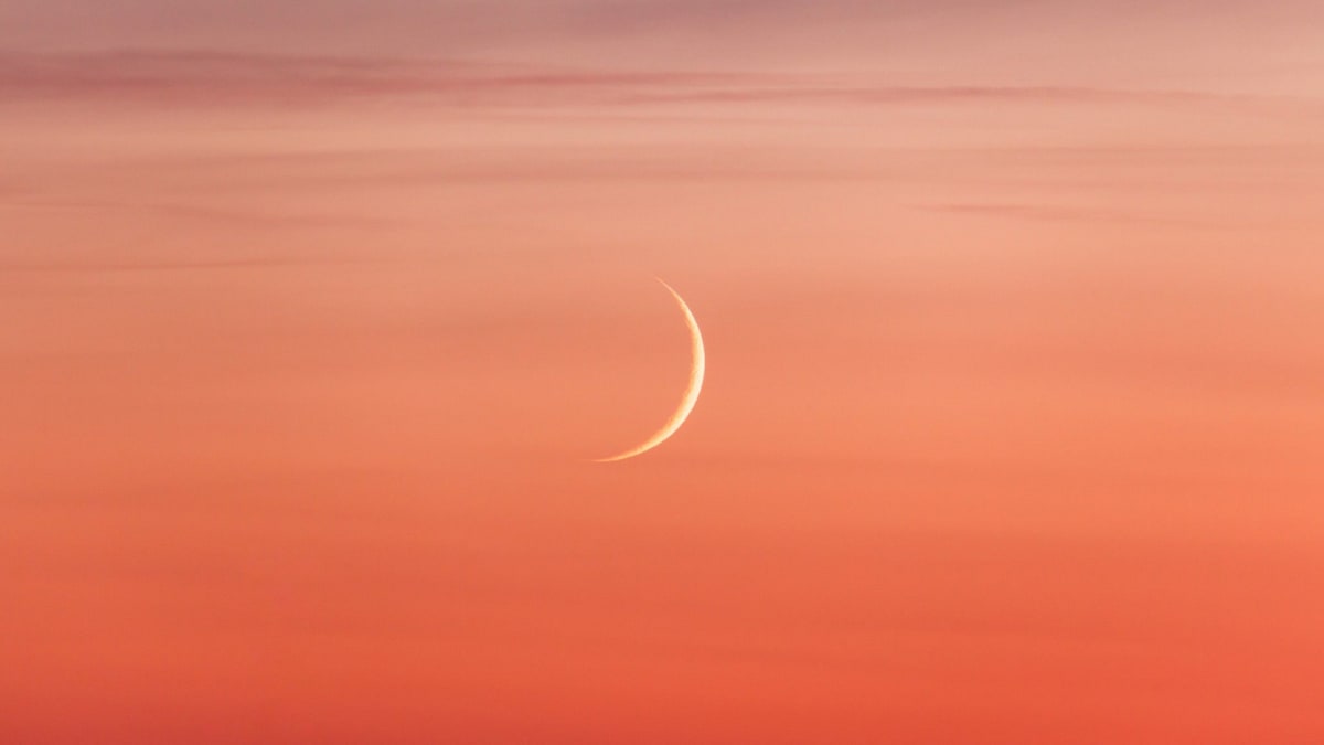 Thin crescent moon hanging low in twilight sky near brilliant Venus above western horizon