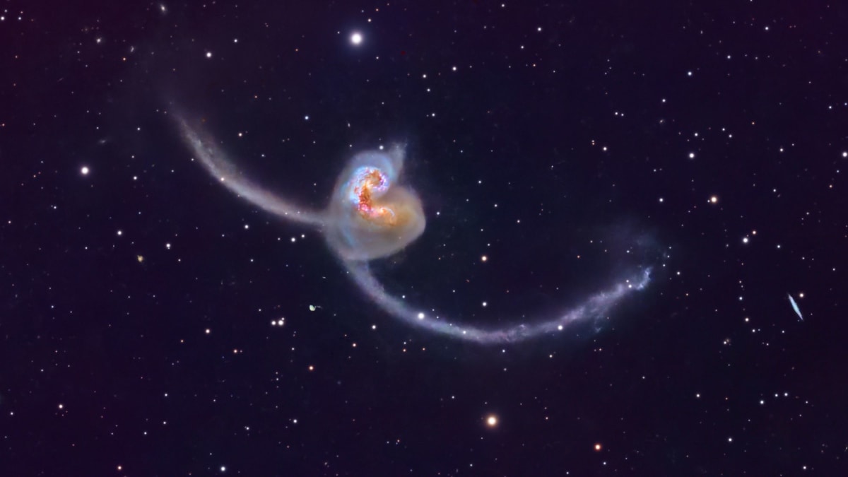 Two colliding spiral galaxies with orange cores and sweeping antenna-like arms against deep space