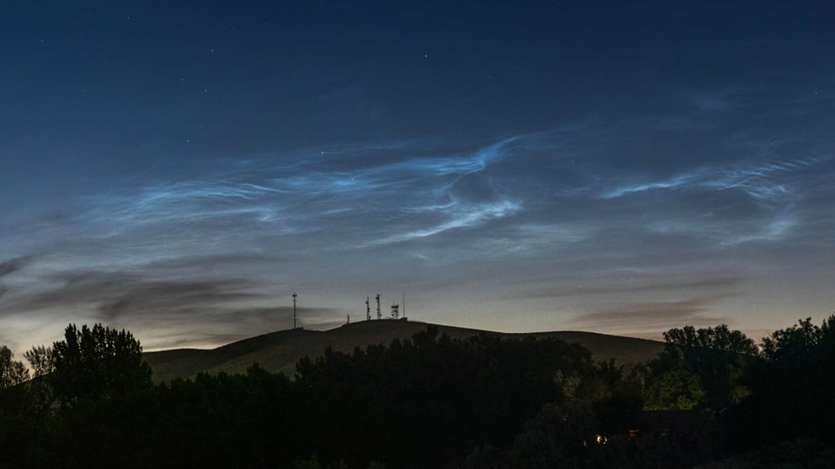 ** Silvery blue noctilucent clouds glowing against twilight sky above mountain silhouette in Washington State