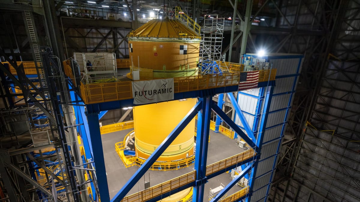 Tall orange rocket core stage stands vertical inside NASA's massive Vehicle Assembly Building