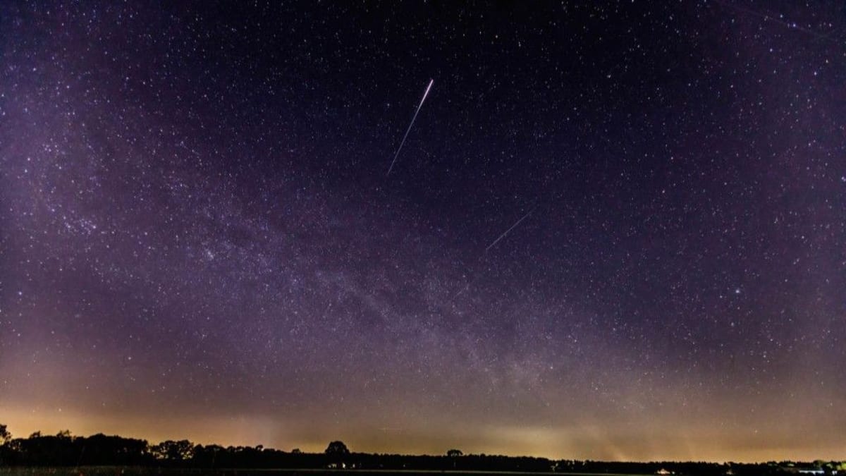 Bright Lyrid meteor streaking across starry night sky above dark landscape
