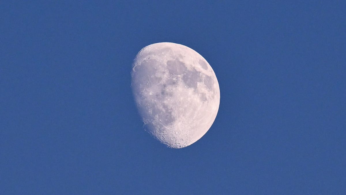 Waxing crescent moon glowing bright against blue daytime sky over landscape