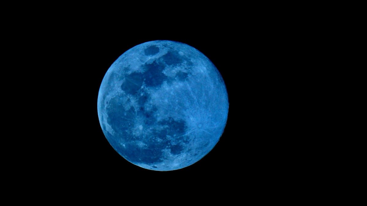 Full moon glowing bright against dark night sky reflecting blue light
