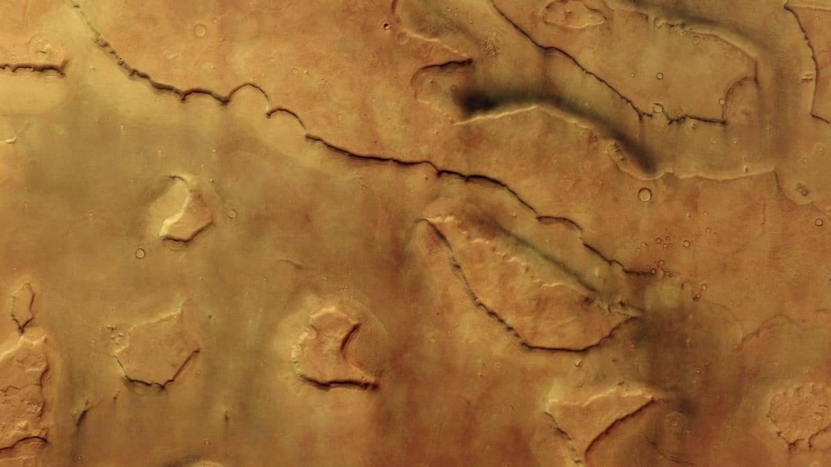 Aerial view of Mars' Mamers Valles showing red valleys with yellow dust devils and pink shadows