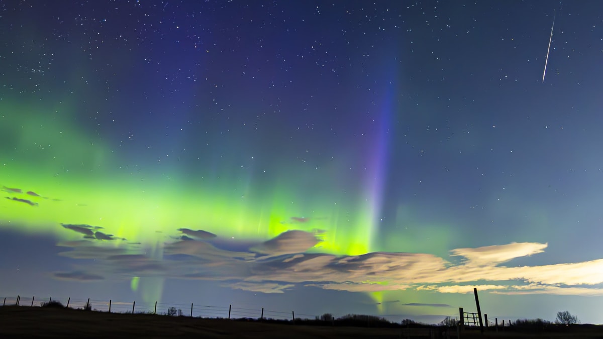 Bright Lyrid meteor streaking downward against green and blue northern lights over Alberta, Canada