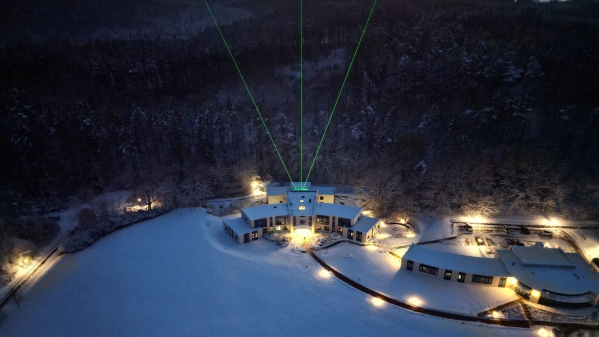 Three green laser beams shooting upward into night sky from atmospheric research institute in winter