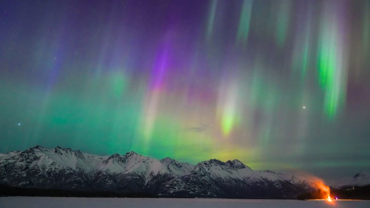 ** Vibrant green and pink aurora borealis dancing above snow-covered mountains in Fairbanks, Alaska at night