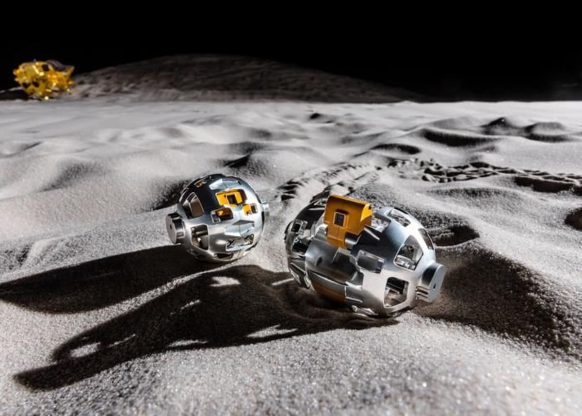 Spherical LEV-2 robot with metal wheels traversing moon's dusty surface near spacecraft
