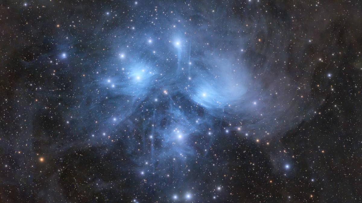 The Pleiades star cluster glowing bright blue surrounded by ghostly reflection nebulas in deep space