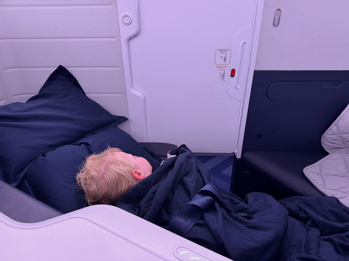 Young child sleeping peacefully in reclined airplane seat wearing blue pajamas during overnight flight