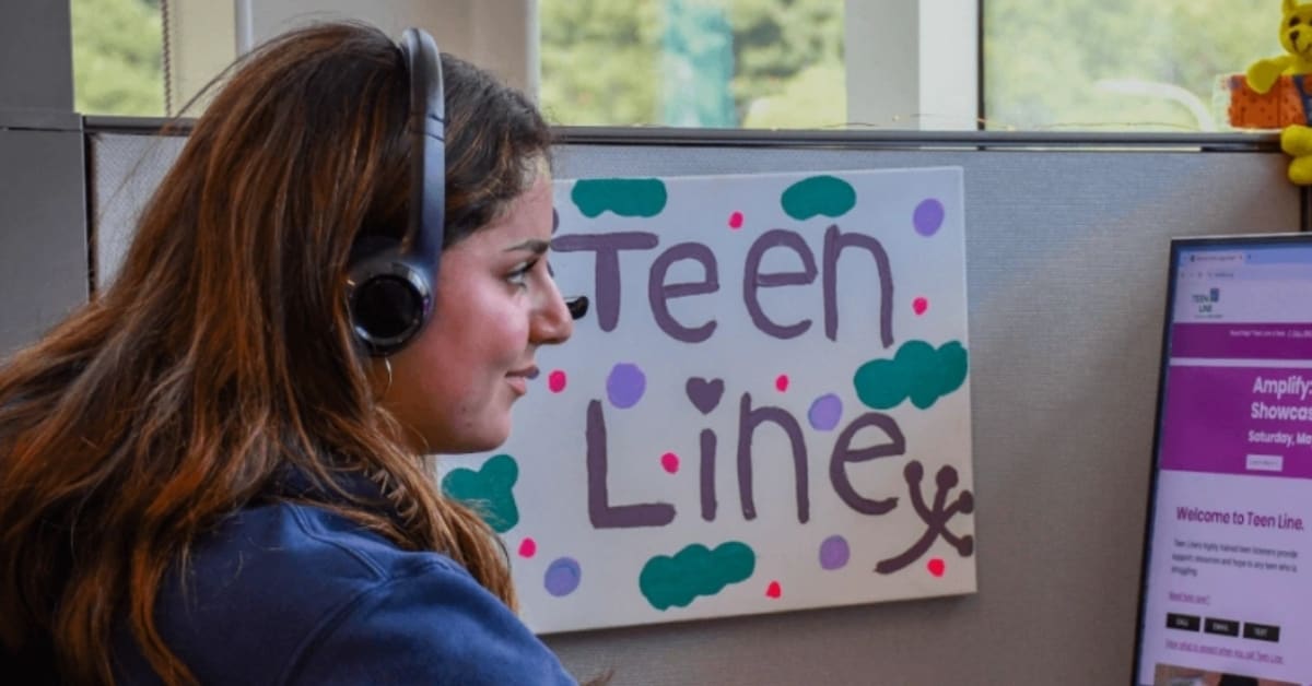 Teen volunteer wearing headphones smiles while answering crisis hotline call at Teen Line desk