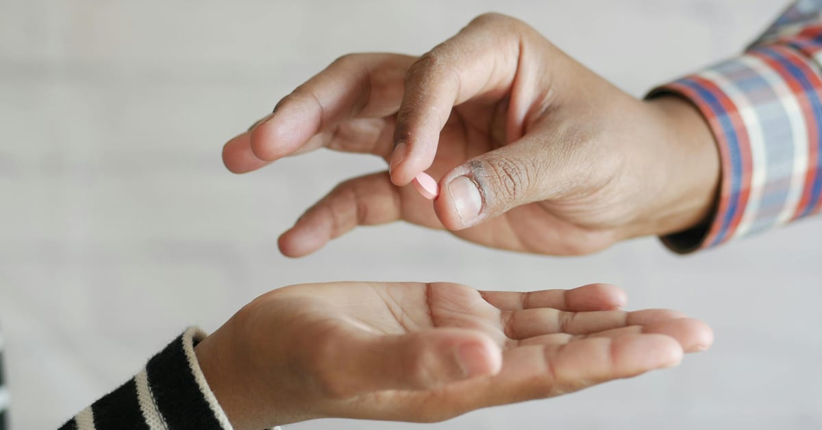 Paper bag containing contraceptive supplies being handed between two people on university campus sidewalk