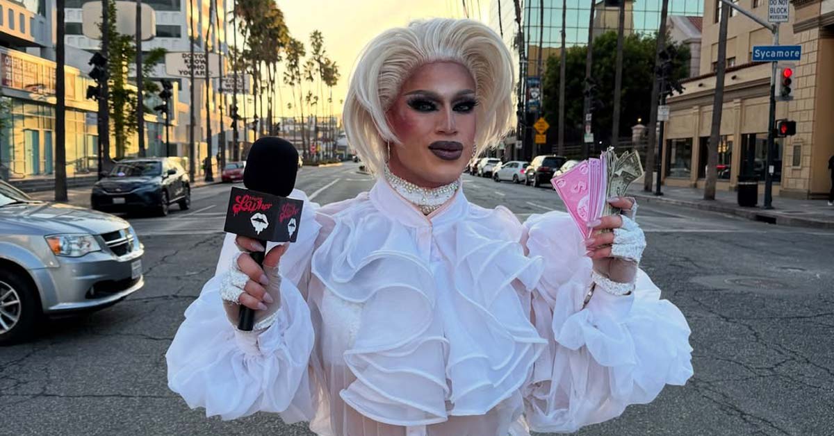 Drag queen Jessica L'Whor in full makeup and costume holding sign reading Ask A Queen Anything