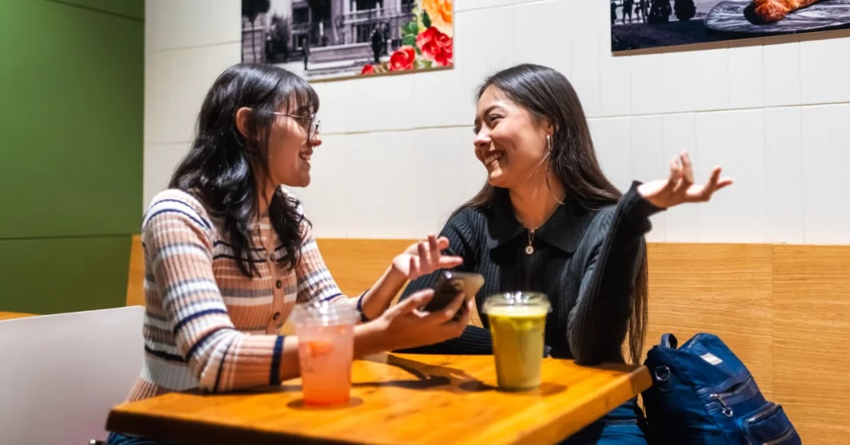 Two friends laughing together over coffee at a casual outdoor cafe