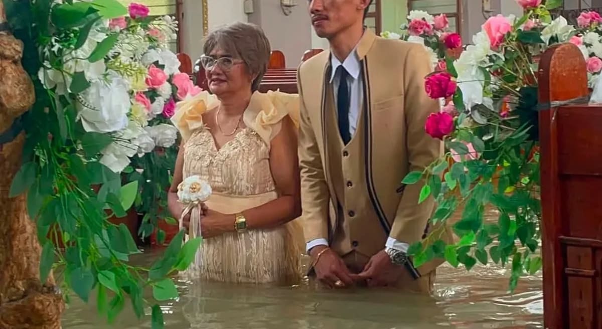 Bride in white gown and groom wade through brown floodwater inside Philippine church during wedding ceremony