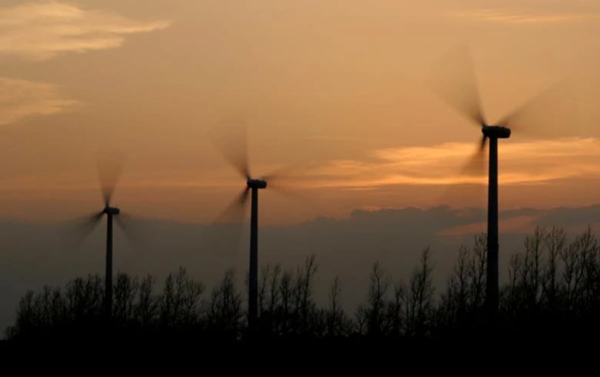 Modern white wind turbines spinning against blue sky with large battery storage facility in Chilean landscape