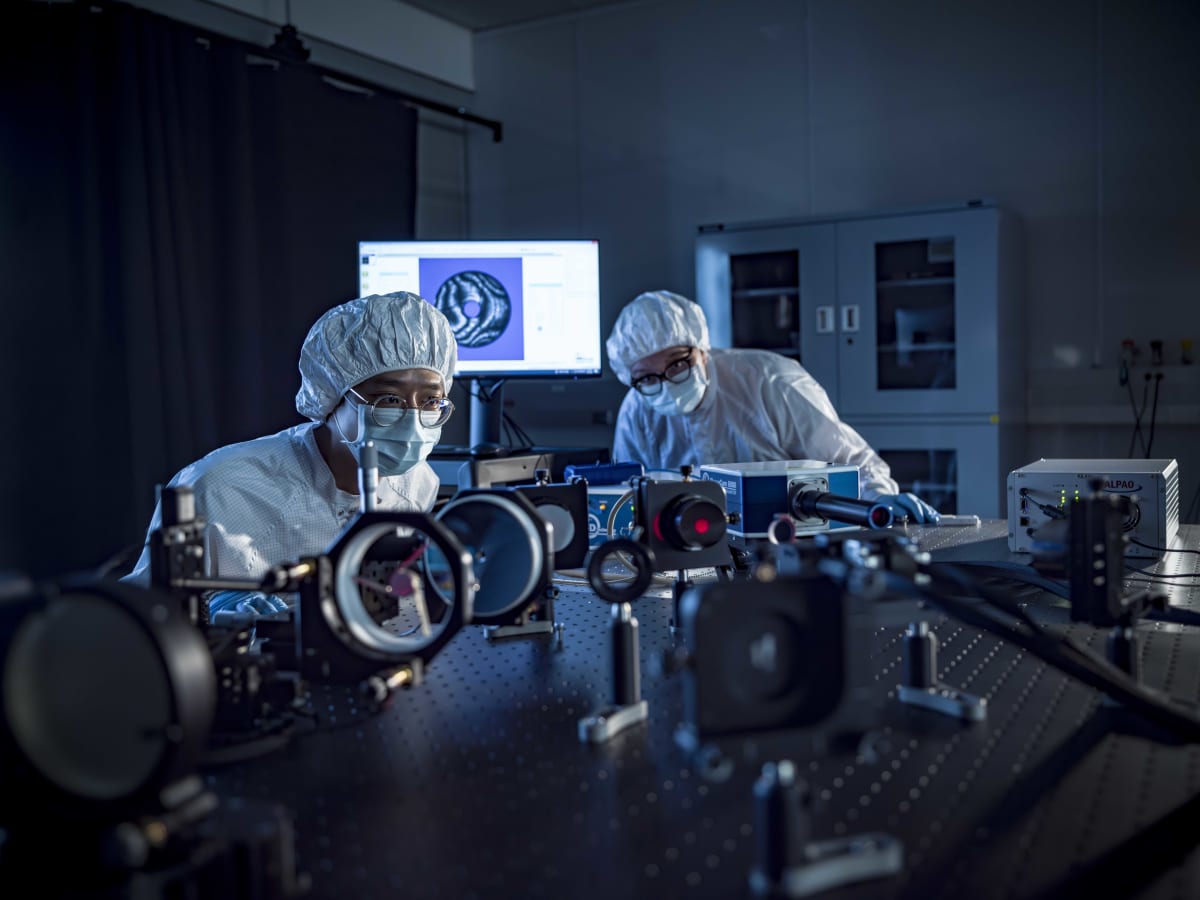 Researchers in clean room suits align optical instruments for space telescope testing