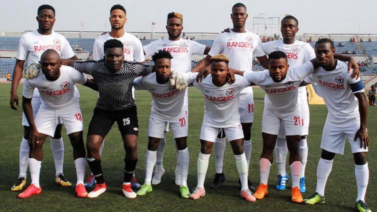 ** Enugu Rangers football team celebrating on field with trophy and supporters cheering
