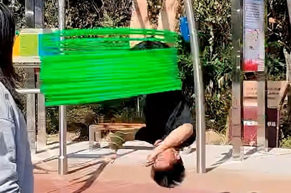 Man hanging upside down from playground equipment spinning multiple hula hoops around waist