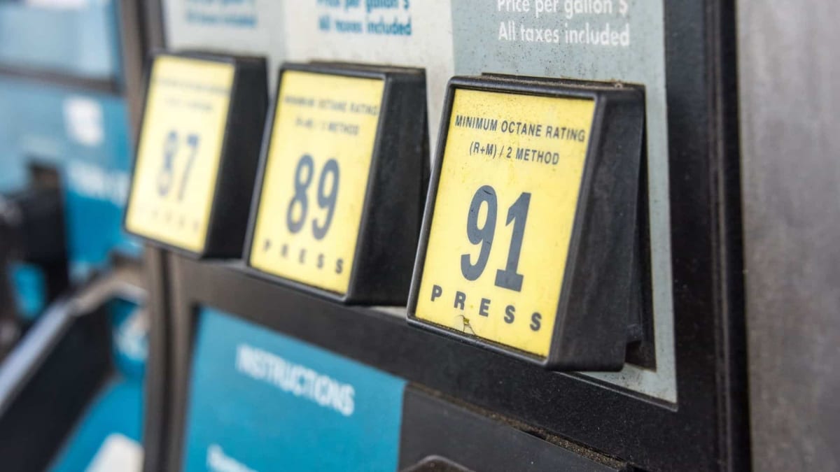 White electric USPS mail delivery truck charging at station with postal worker nearby