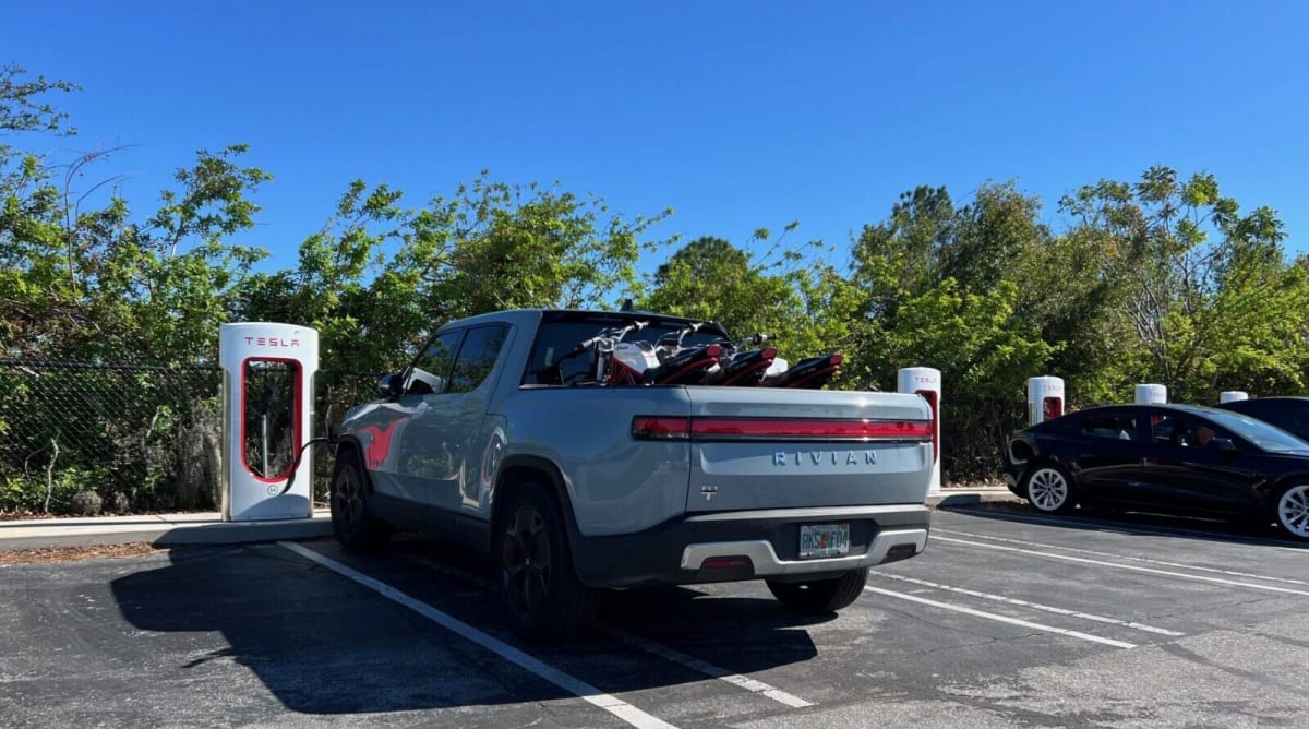 Tesla electric vehicle charging at a supercharger station with multiple charging stalls visible