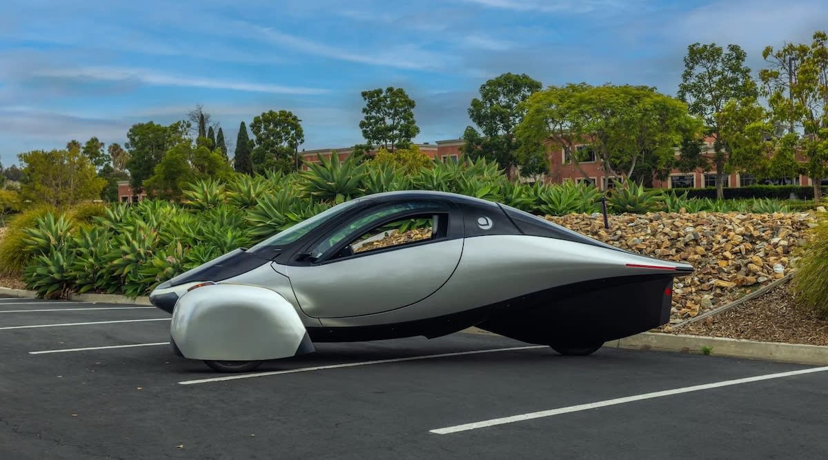 Sleek white three-wheeled Aptera electric vehicle with curved body covered in integrated solar panels