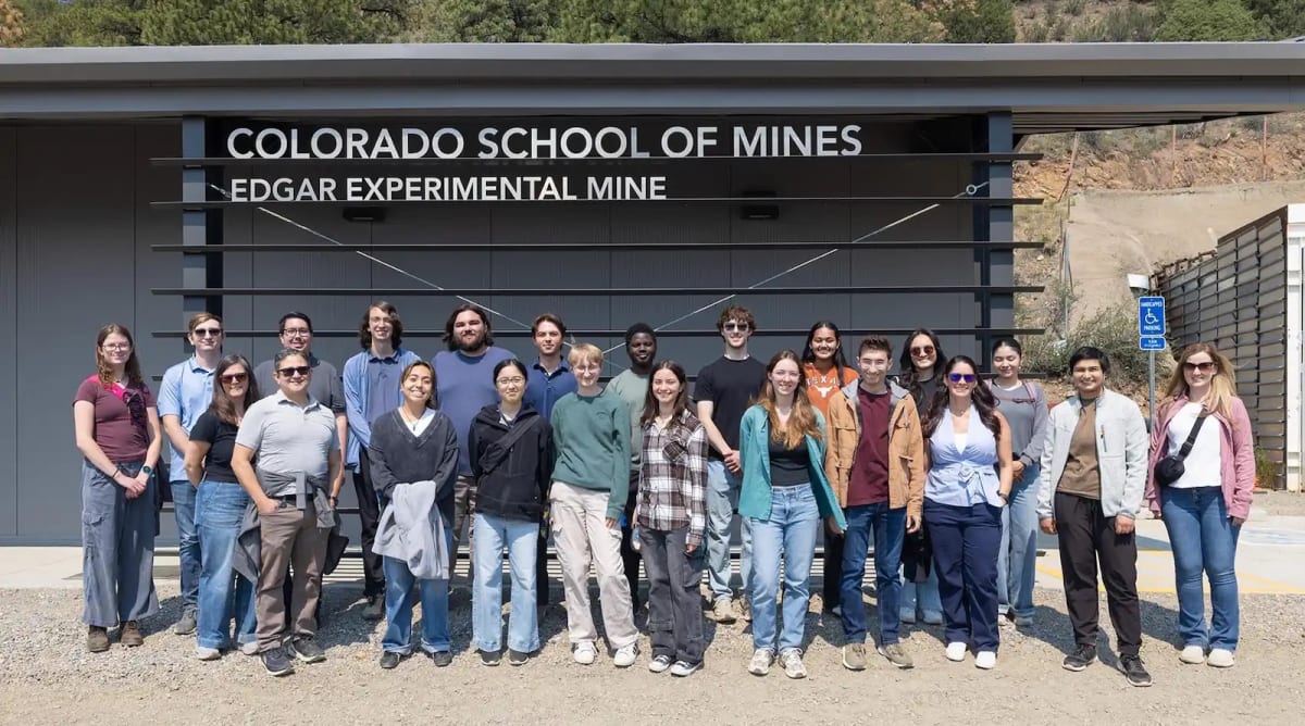 Young interns wearing hard hats explore underground mine tunnel in Colorado mountains