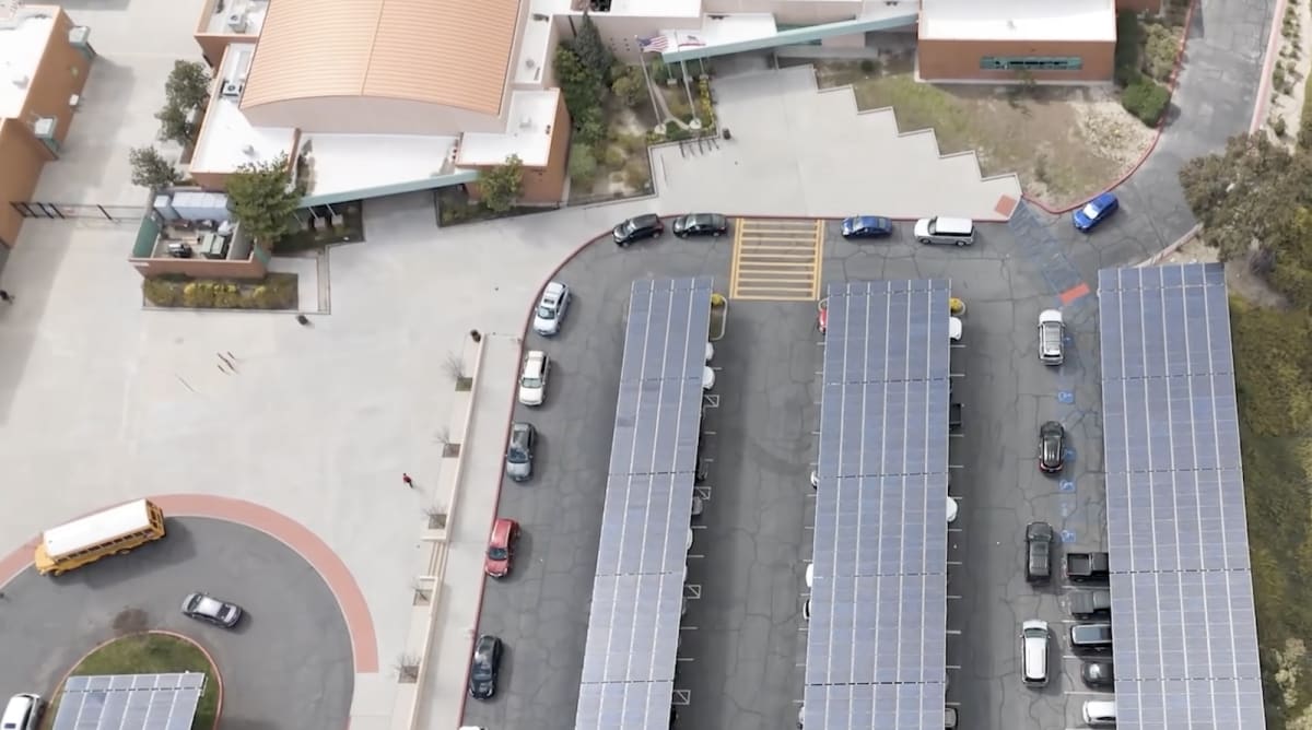 Solar panels installed on school rooftop with students visible in courtyard below