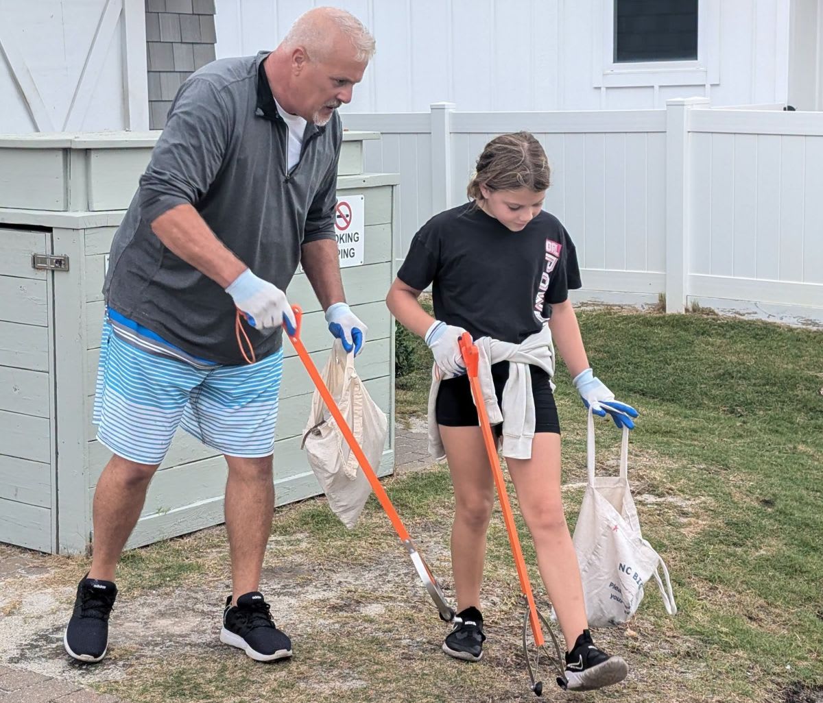 Students in school gear collecting trash and debris along Kure Beach shoreline with cleanup supplies