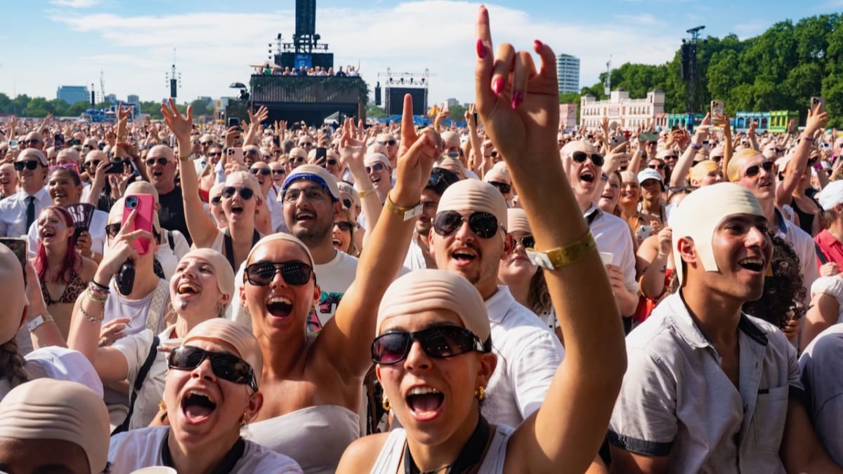 Thousands of concert fans wearing shiny bald caps at outdoor music festival in London