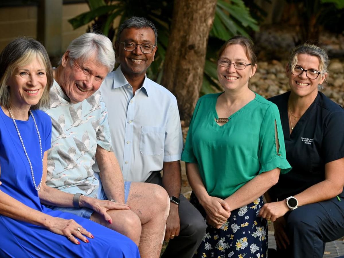 ** Elderly man embracing hospital ICU staff members during grateful reunion visit
