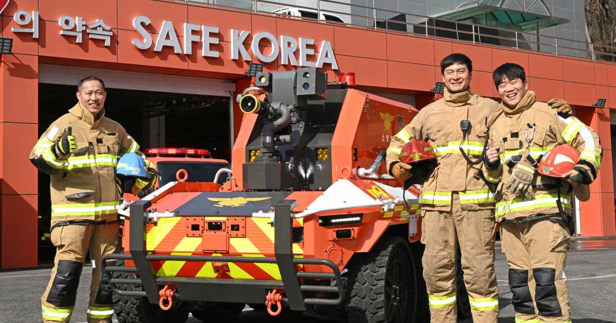 Bright red autonomous firefighting robot with hose system and thermal cameras beside firefighters