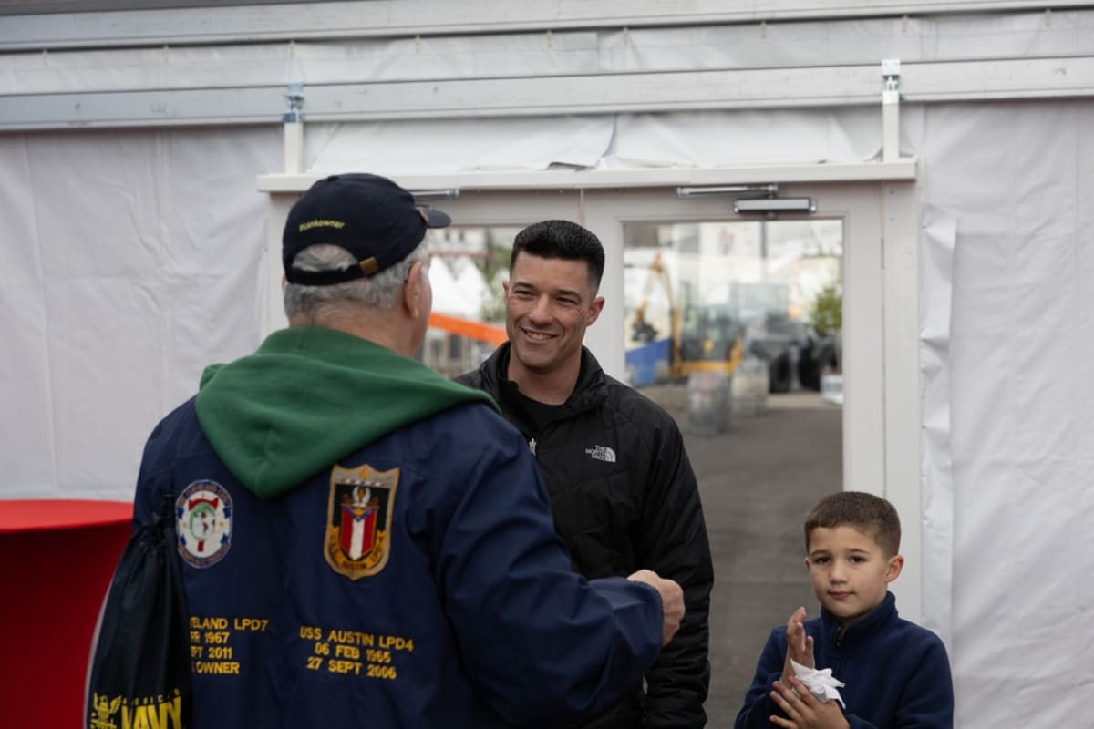 Navy commander speaking with elderly veterans wearing service caps at ship commissioning event