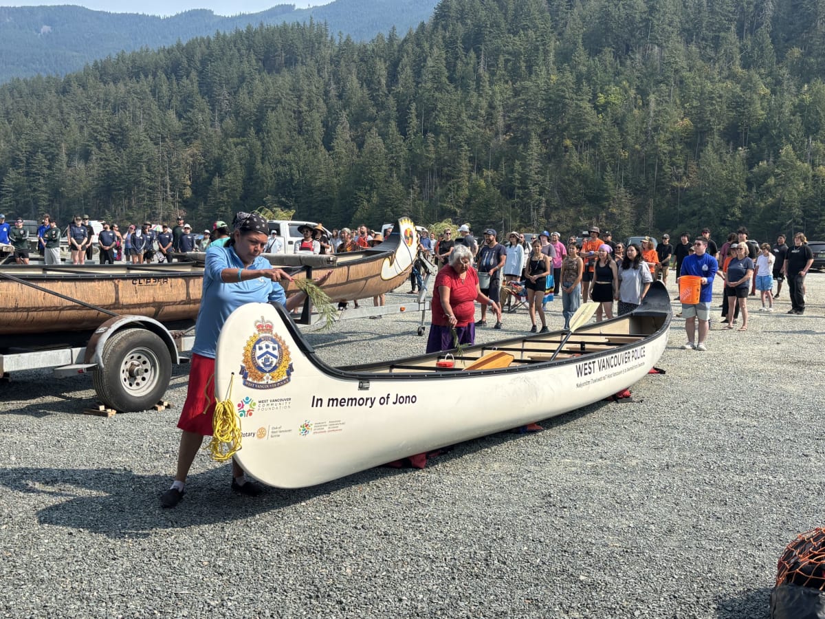 Multiple traditional canoes with paddlers traveling together on calm river waters in British Columbia