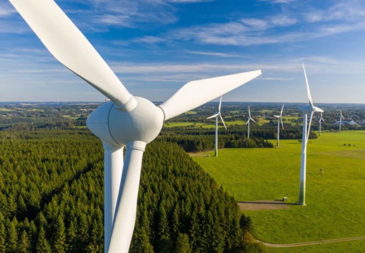 ** Modern white wind turbines spinning against blue sky in rural Germany generating clean renewable energy