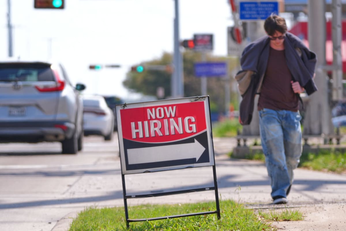 Happy diverse workers shaking hands at job fair with "Now Hiring" signs visible