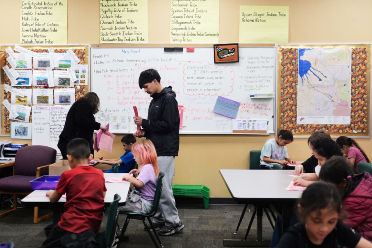 Native American high school student working as teaching assistant with elementary students in classroom