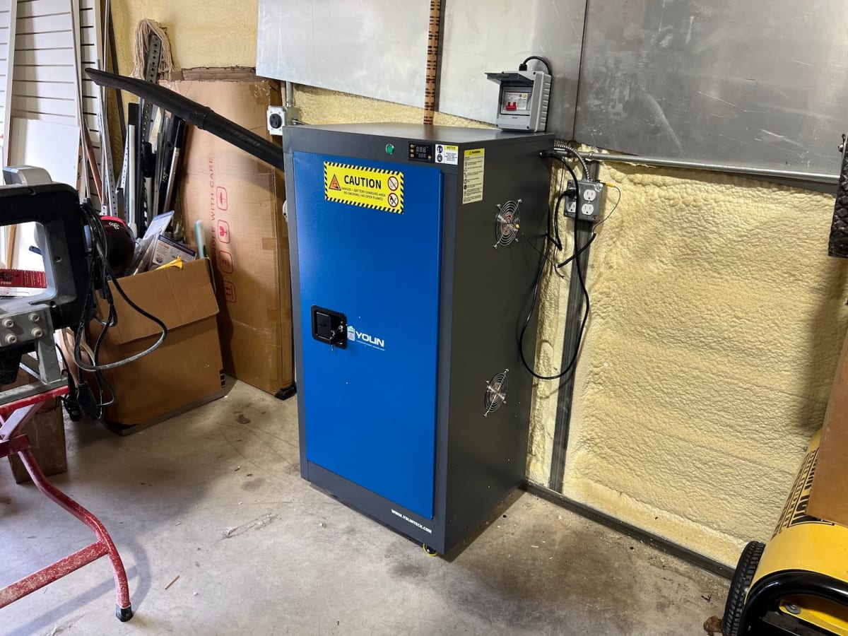 Steel workshop cabinet with open door showing organized e-bike batteries charging on multiple shelves