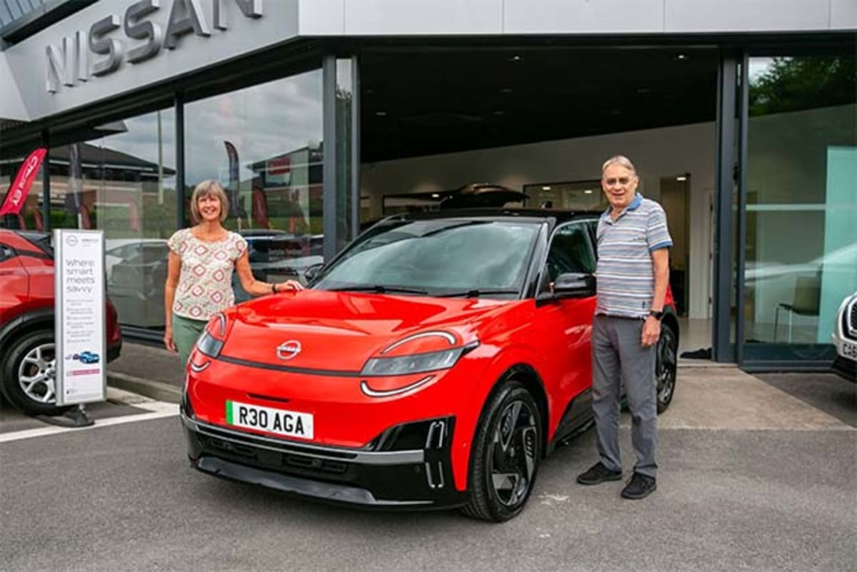 Couple standing next to new white Nissan MICRA electric vehicle at dealership