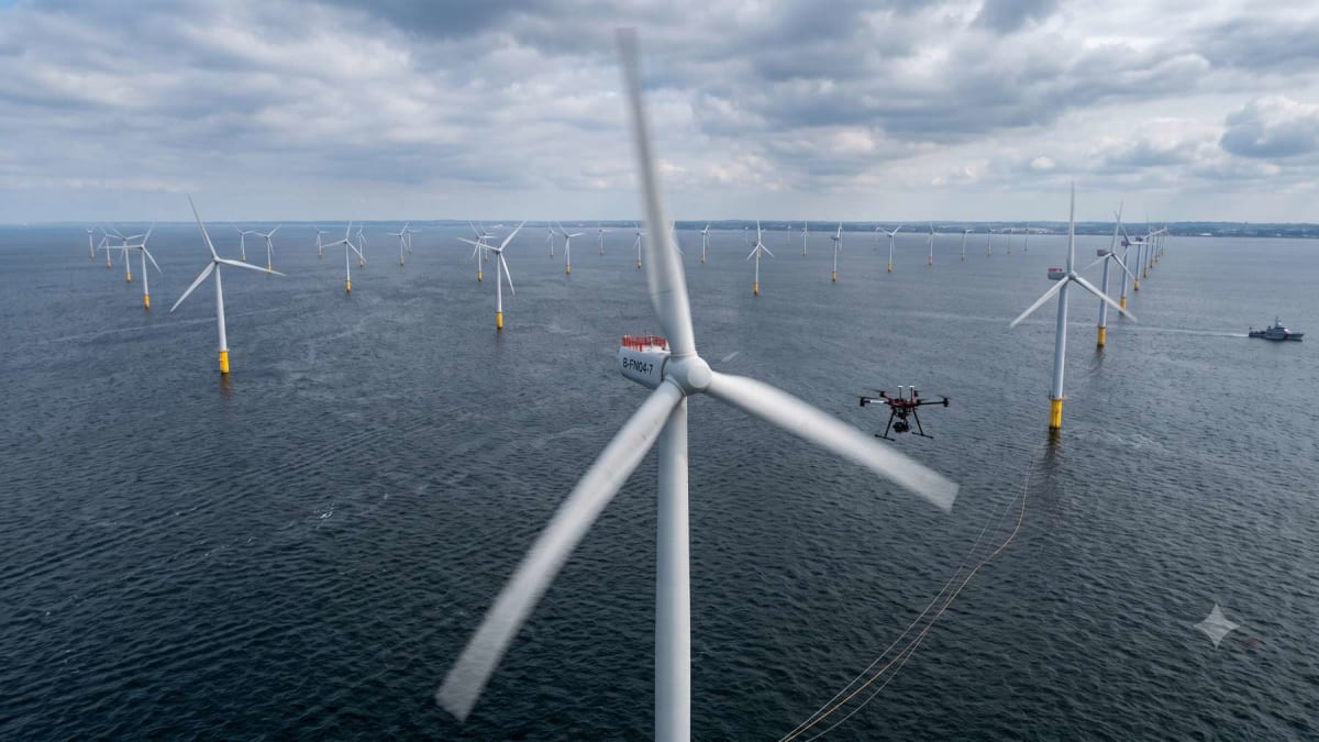 Autonomous drone flying near spinning offshore wind turbine blades over ocean water in Denmark