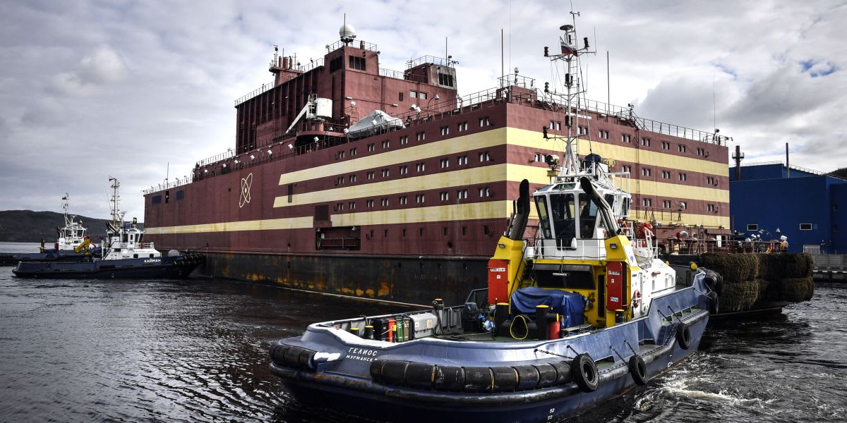 Artist rendering of floating nuclear reactor barge docked near modern container port at sunset