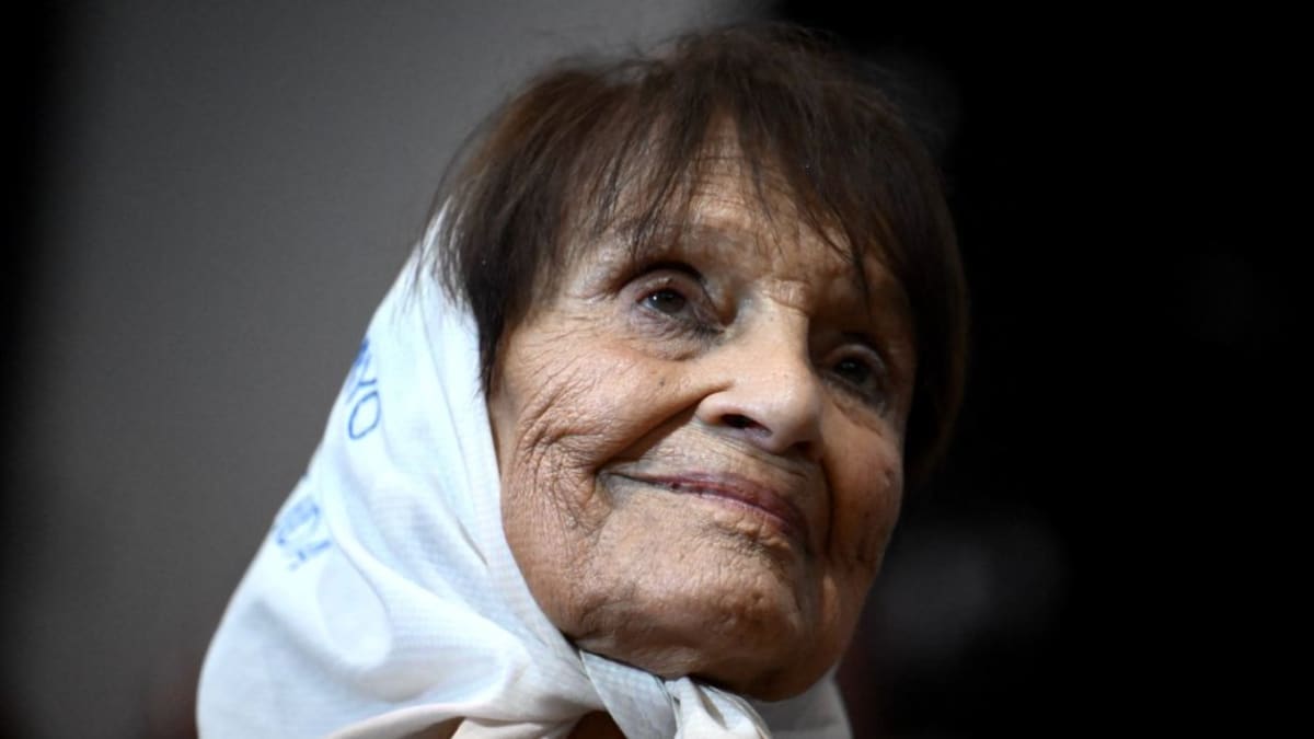 Elderly woman in white headscarf speaking to crowd of young people at memorial rally