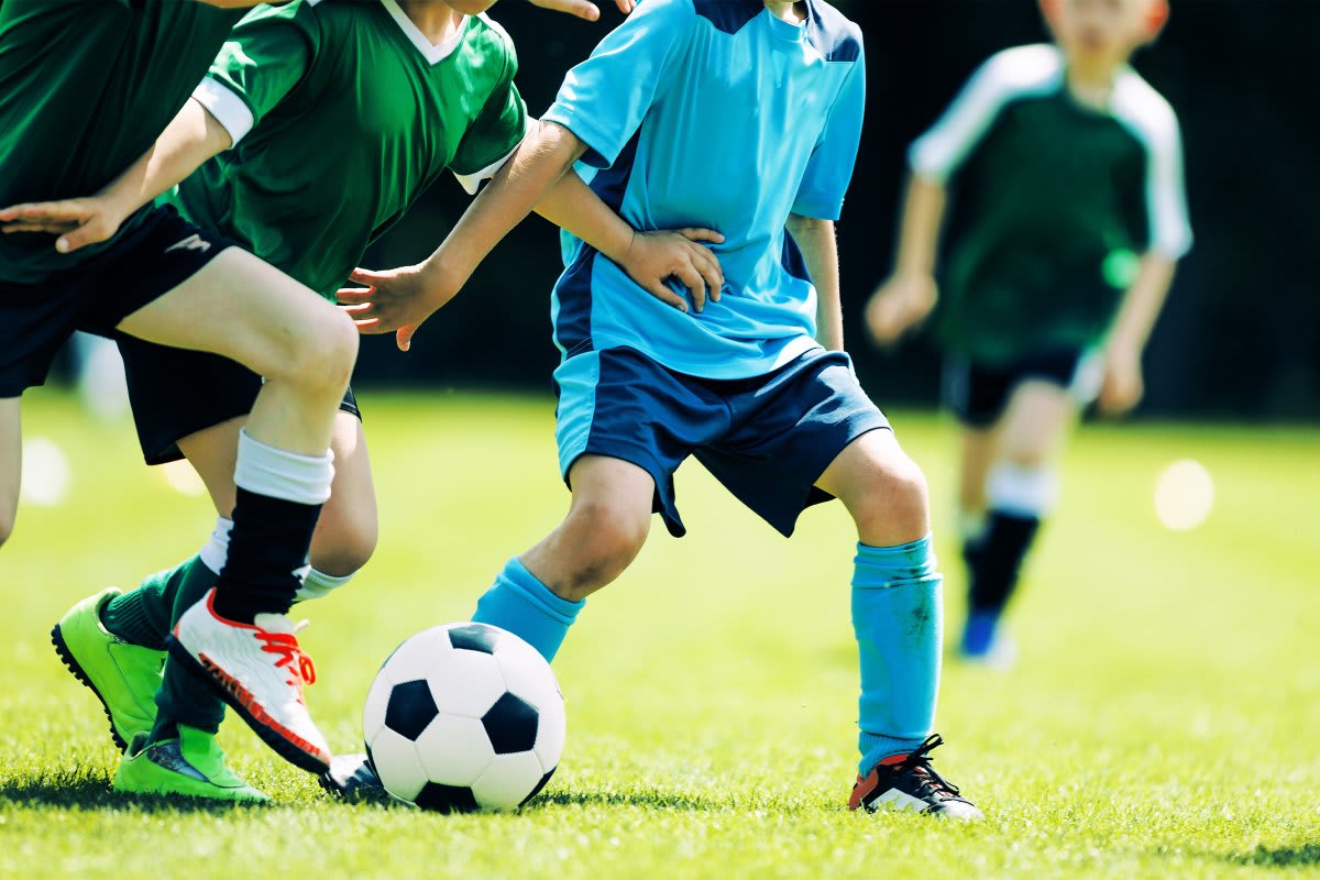 Young soccer players practicing on field while coach observes from sideline